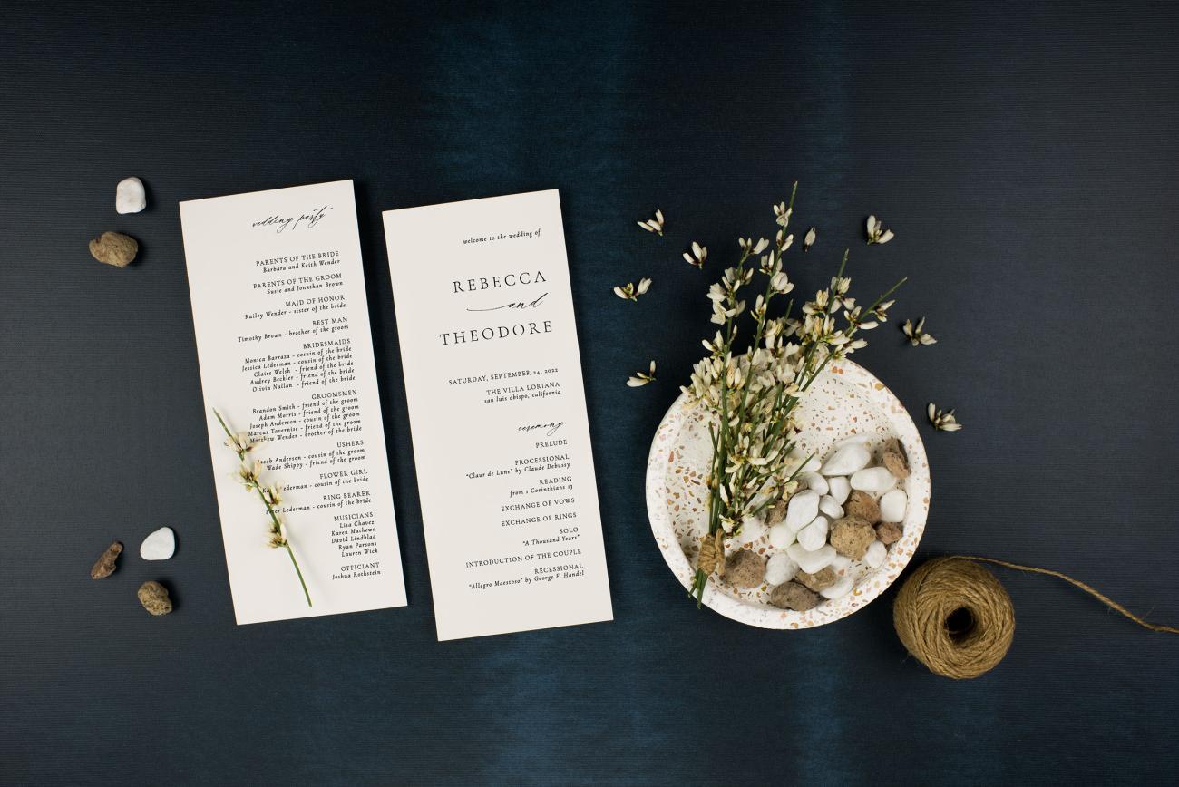 An elegant wedding program sitting on a table with rocks, twine, and pretty flowers