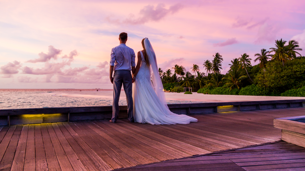 a bride and groom standing on a dock looking at the sunset on their wedding day