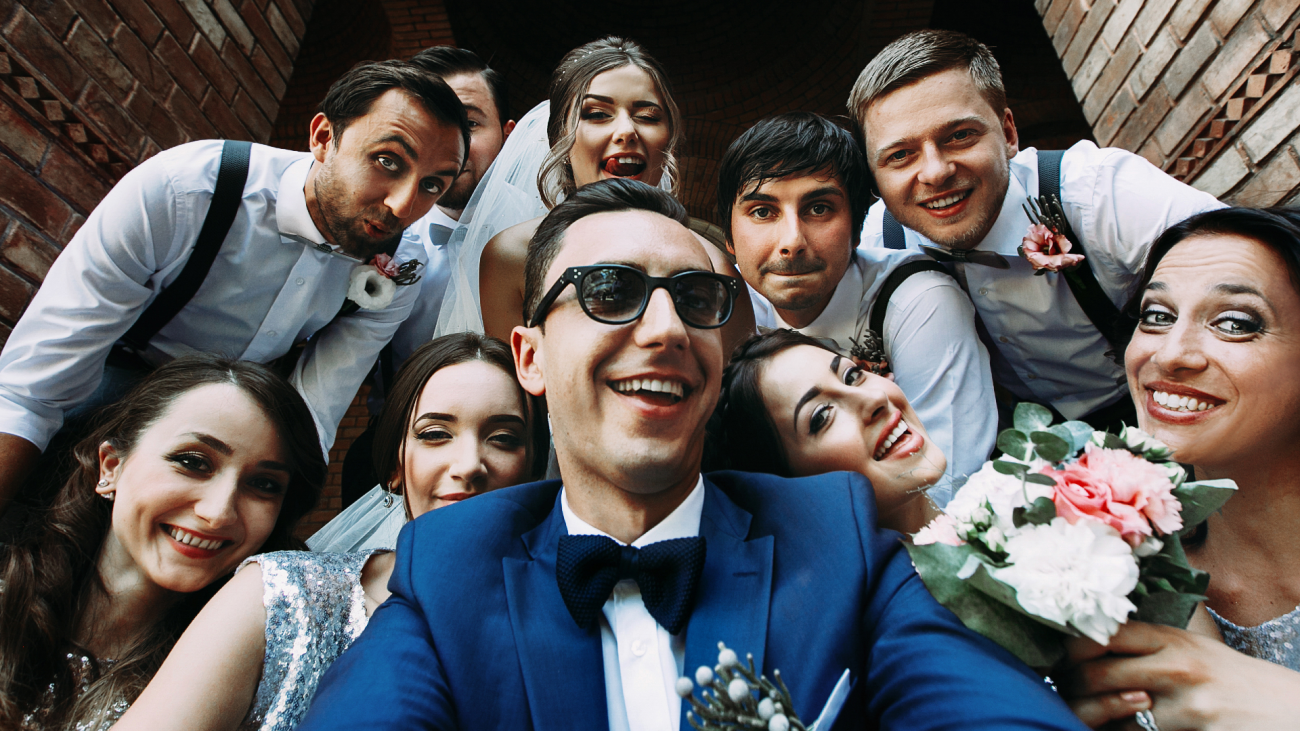 a bride and groom take a selfie with the bridesmaids and groomsmen at their wedding