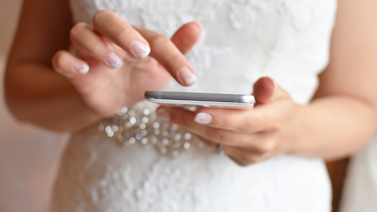 a bride wears a wedding dress and types on a smartphone in her hands