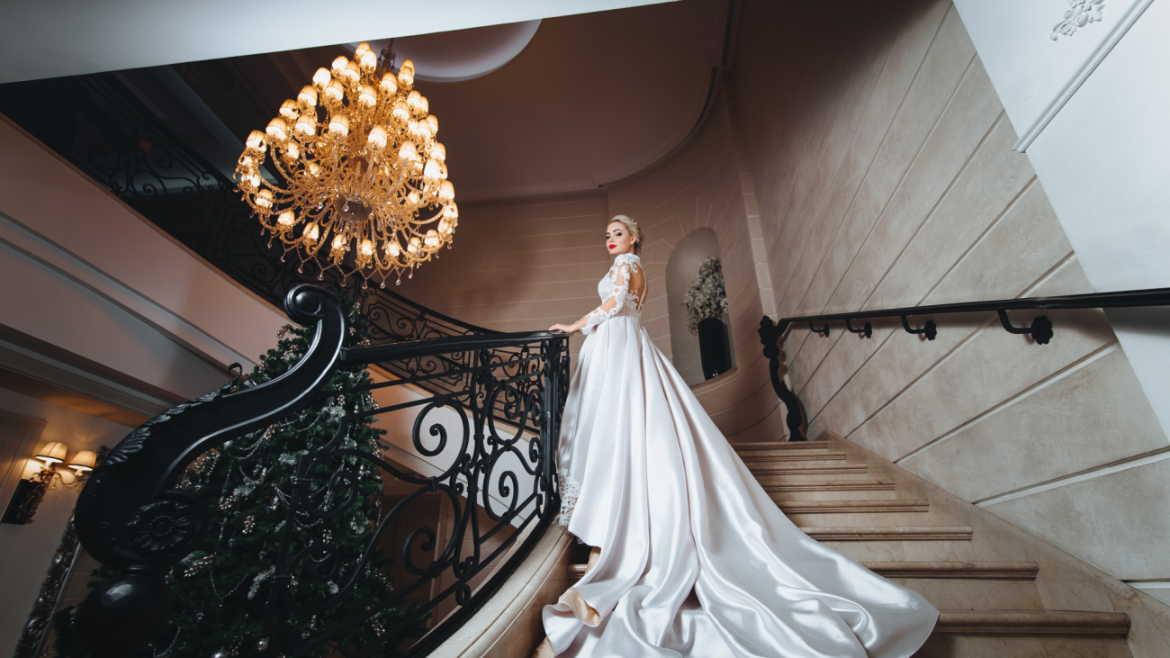 a bride wearing a white wedding dress with a long train climbing up staircase at a wedding venue