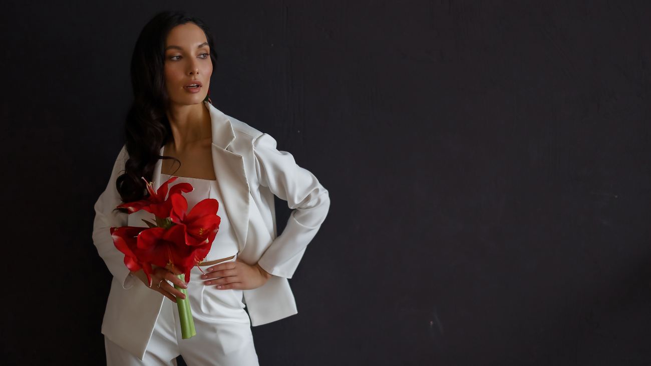 a bride posing in a wedding pantsuit and jacket while holding red flowers