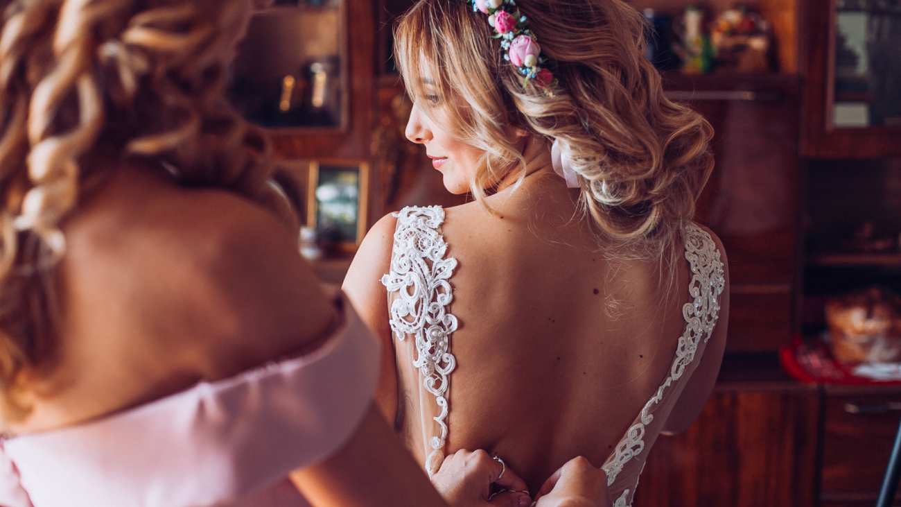a bridesmaid helps a bride button her wedding dress