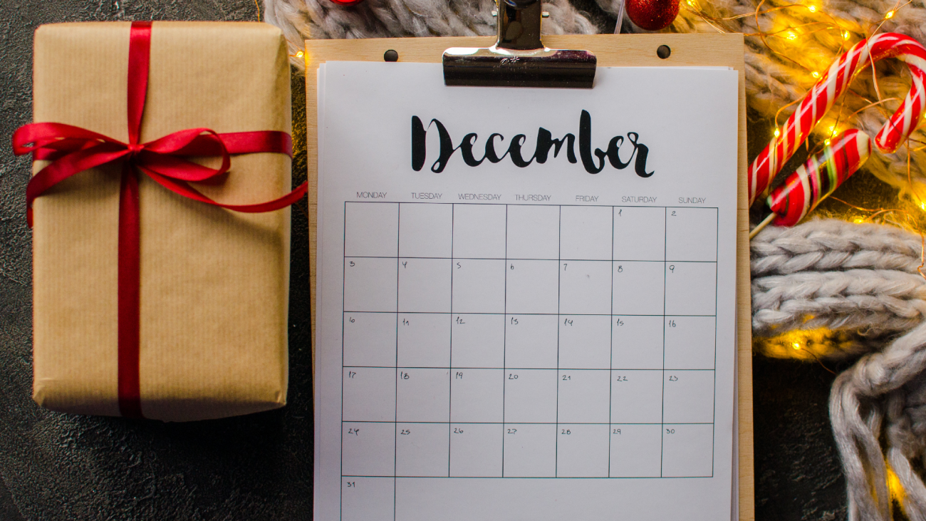 a clipboard with a December calendar clipped on it sits next to a holiday gift
