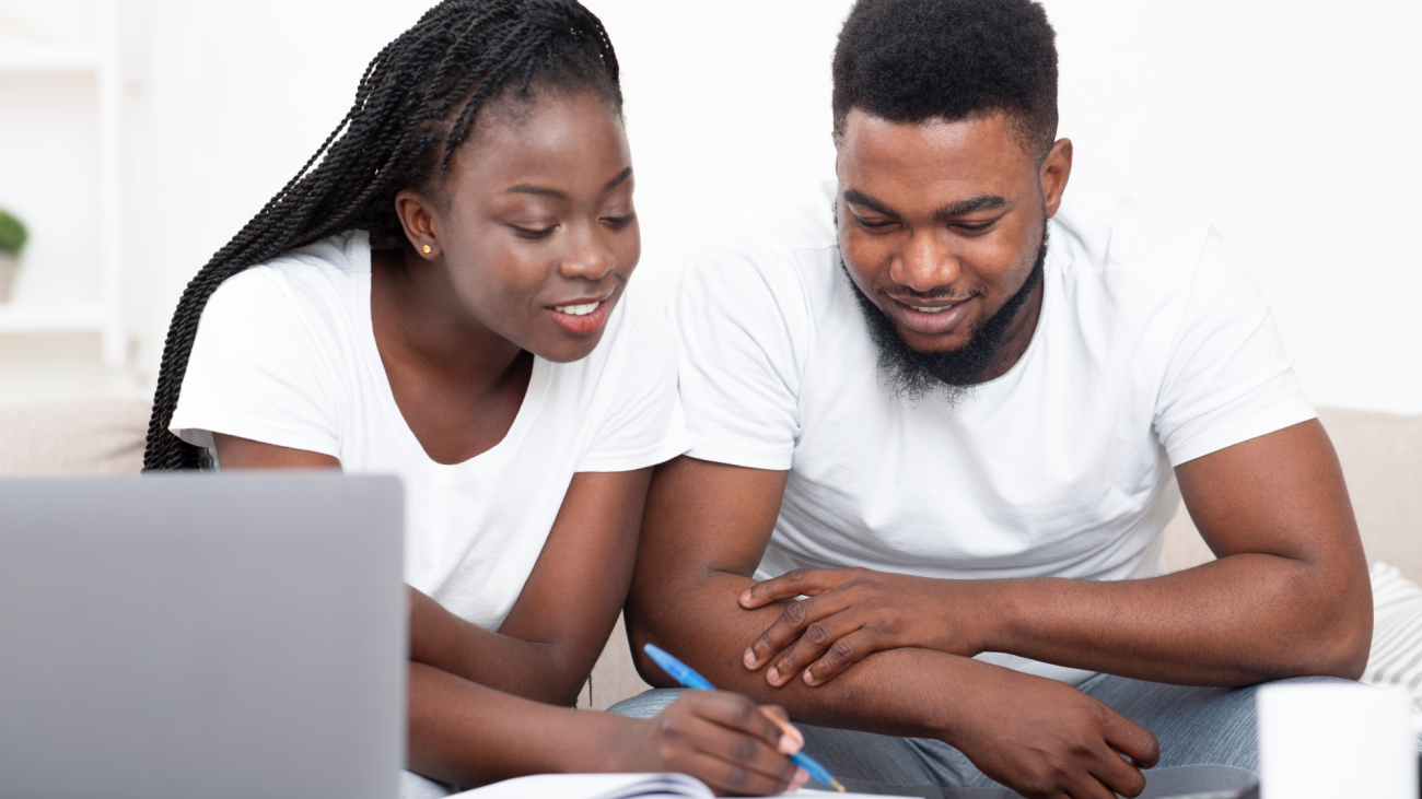a couple looks at a notebook and takes notes while sitting on a couch