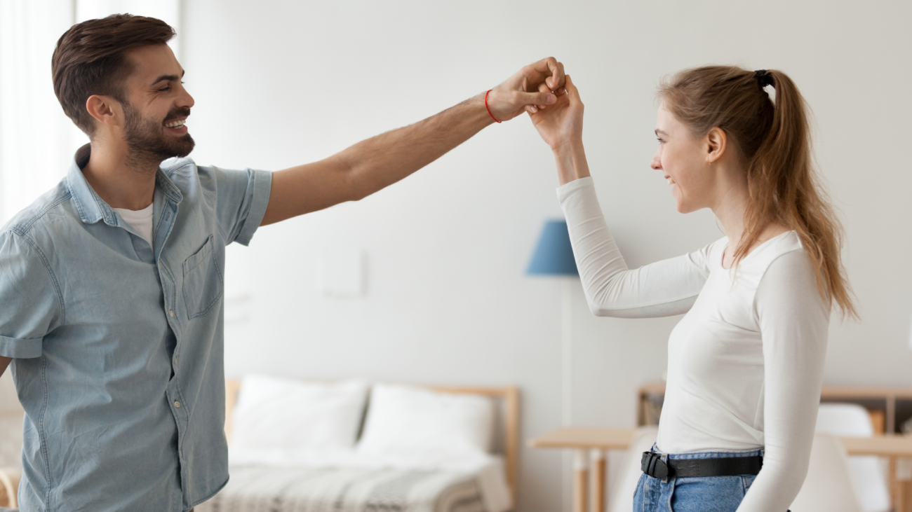 a couple waltzes in their living room together and smiles