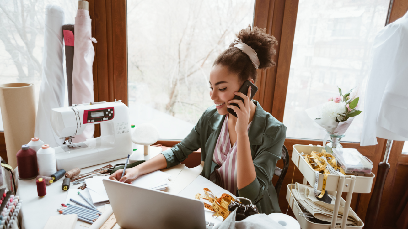 a fashion designer working at her sewing machine while talking on the phone and looking at her laptop computer