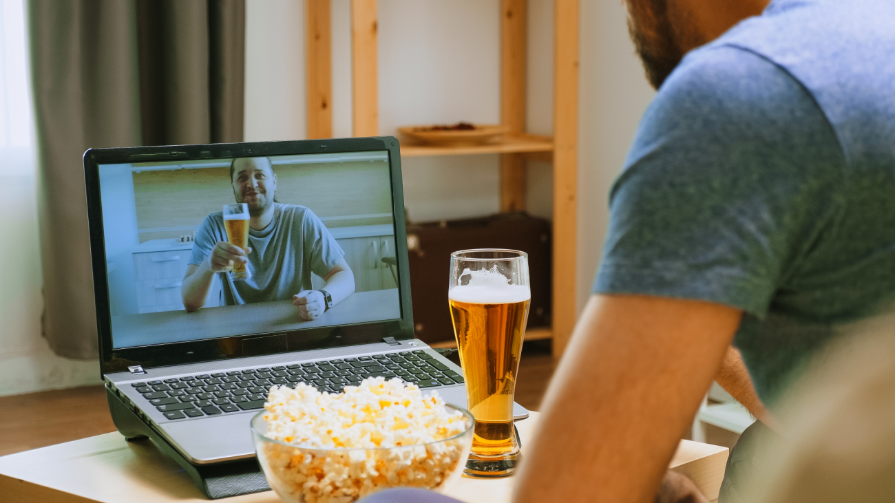 two friends eat popcorn and drink beer in front of their computer screens for socially distanced get together