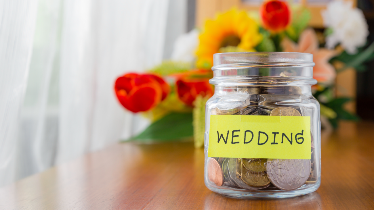 a glass jar filled with coins labeled wedding with bouquet of flowers in the background