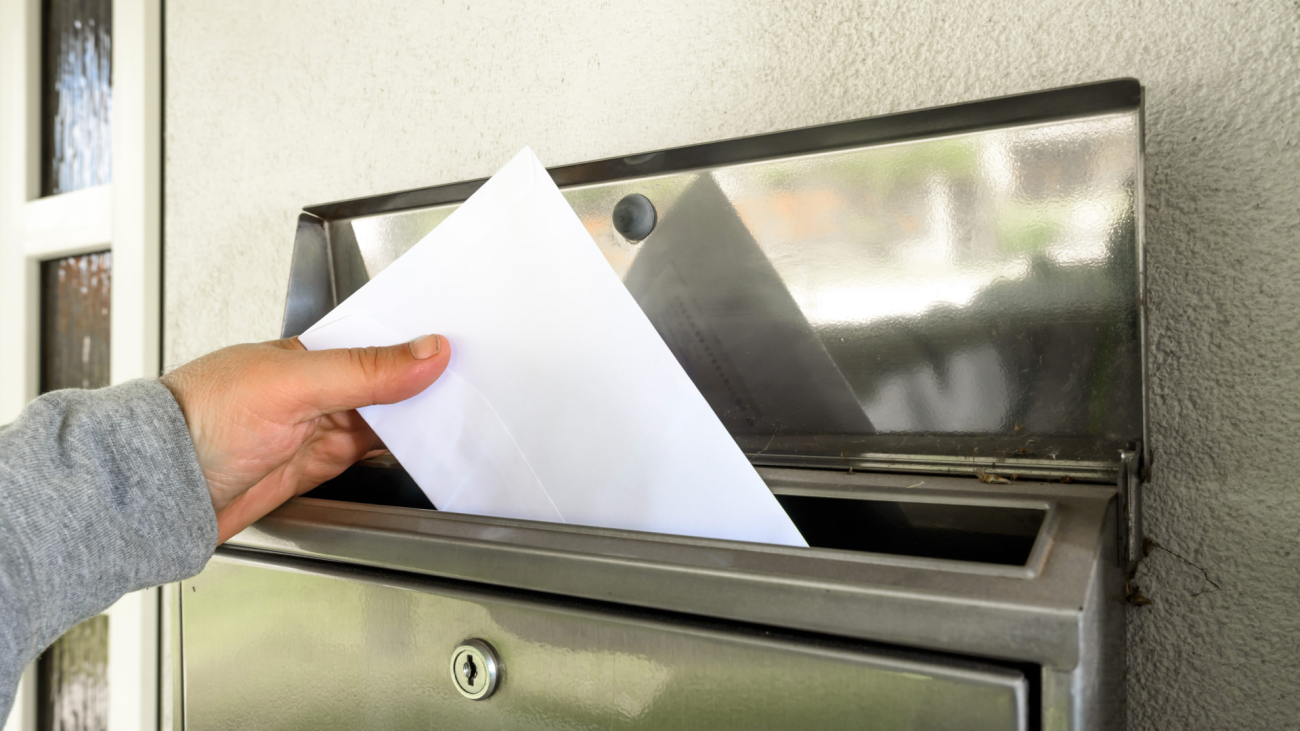 a hand puts mail in a mailbox