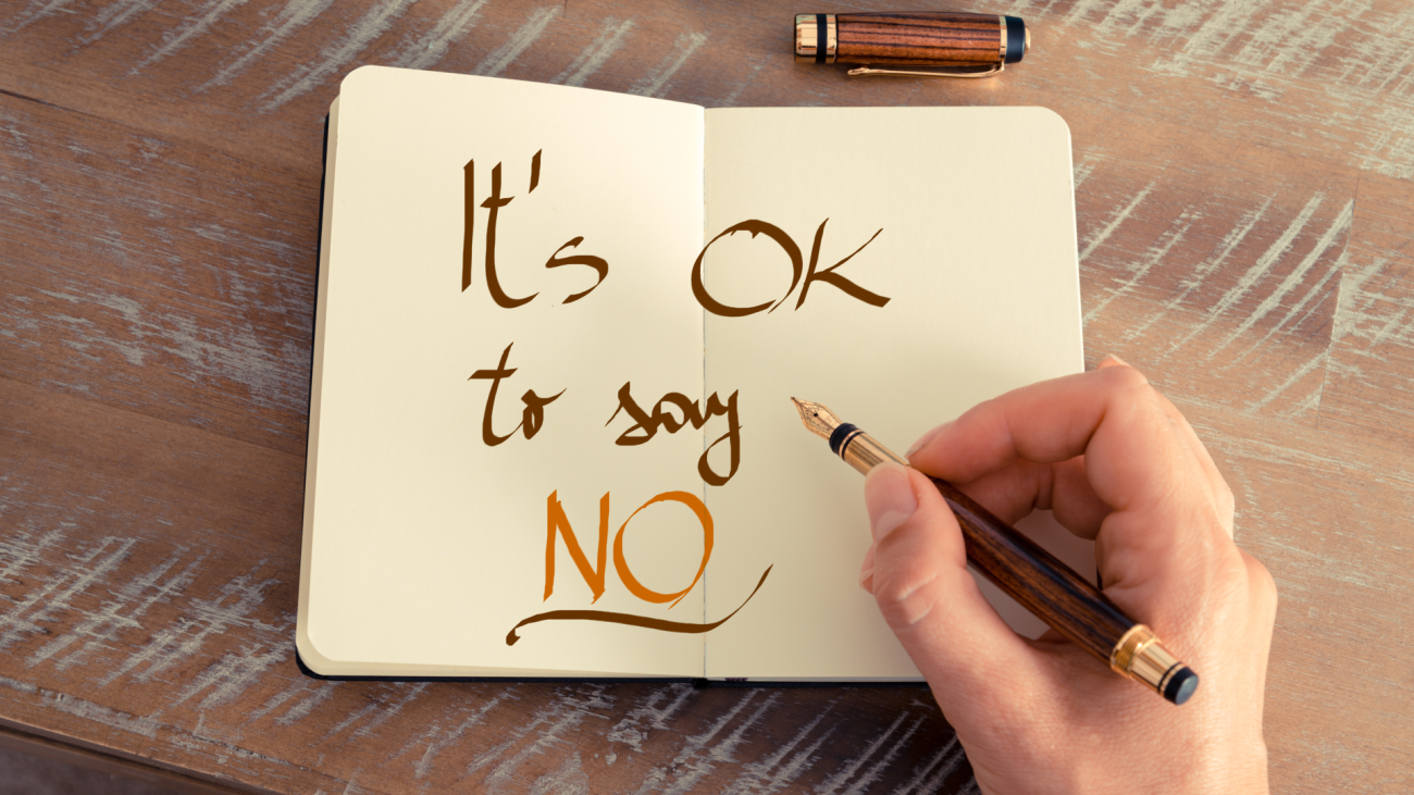 a person’s hand writing “it’s OK to say no” in a notebook