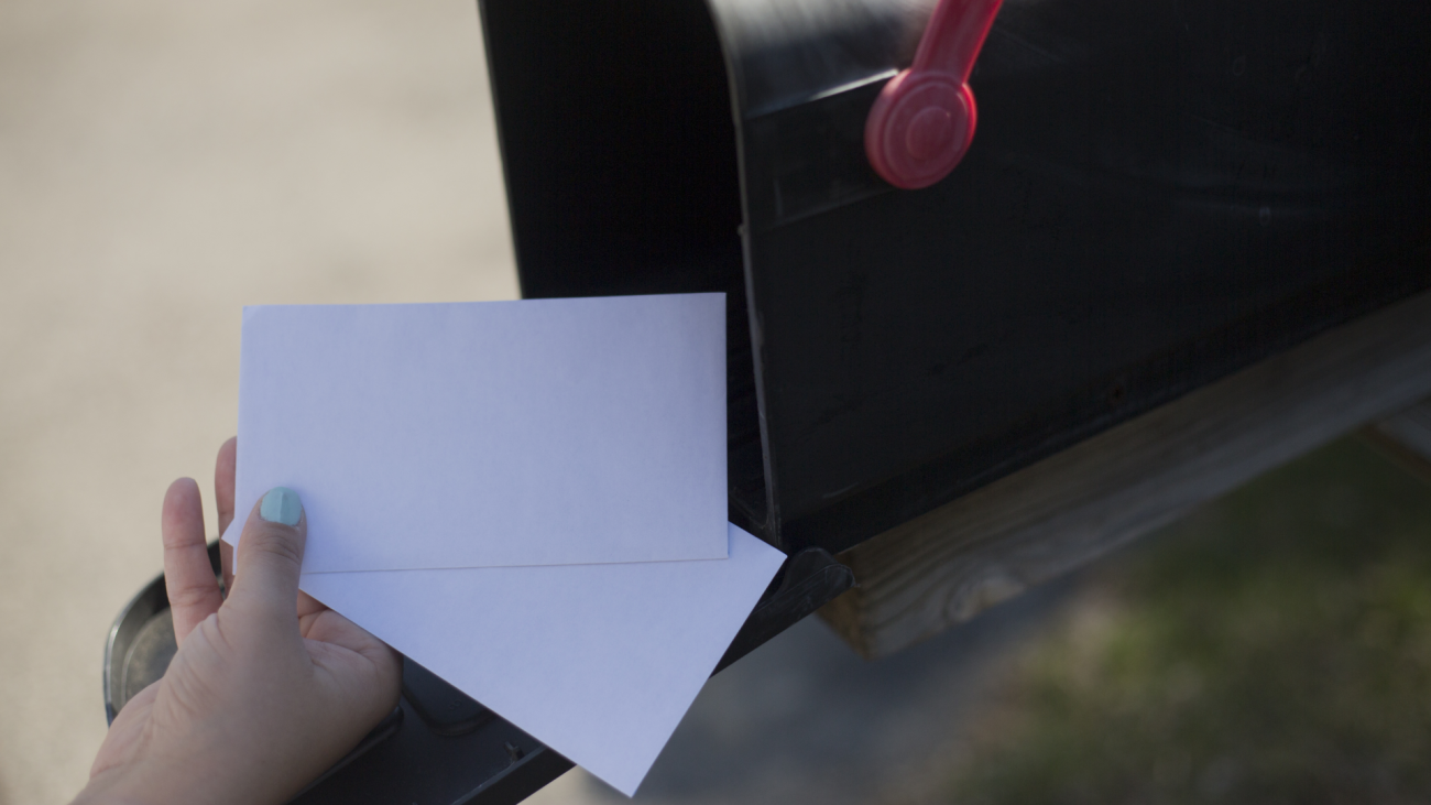 a person’s hands put letters in a mailbox