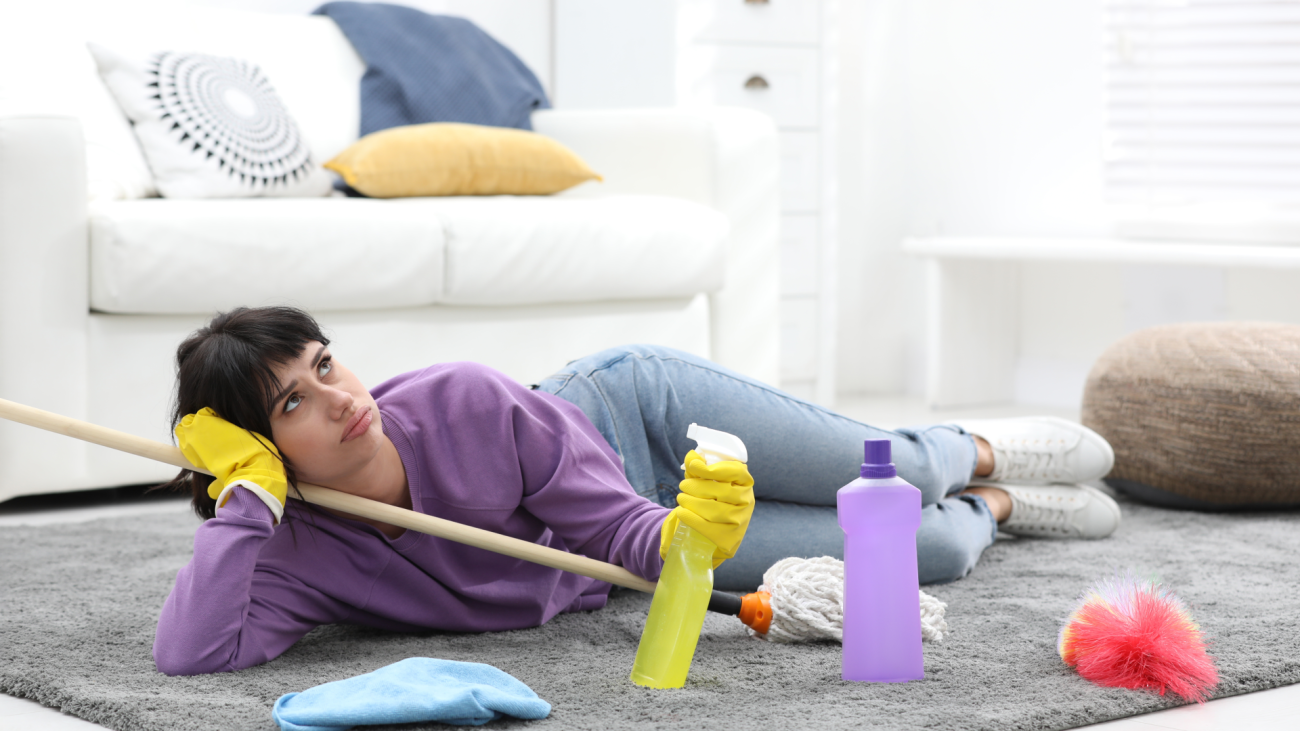 a lazy woman lays on the floor and procrastinates while holding cleaning supplies