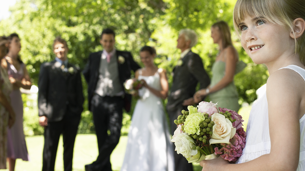 a little girl wearing a white dress holds a bouquet of flowers as wedding guests stand in the background