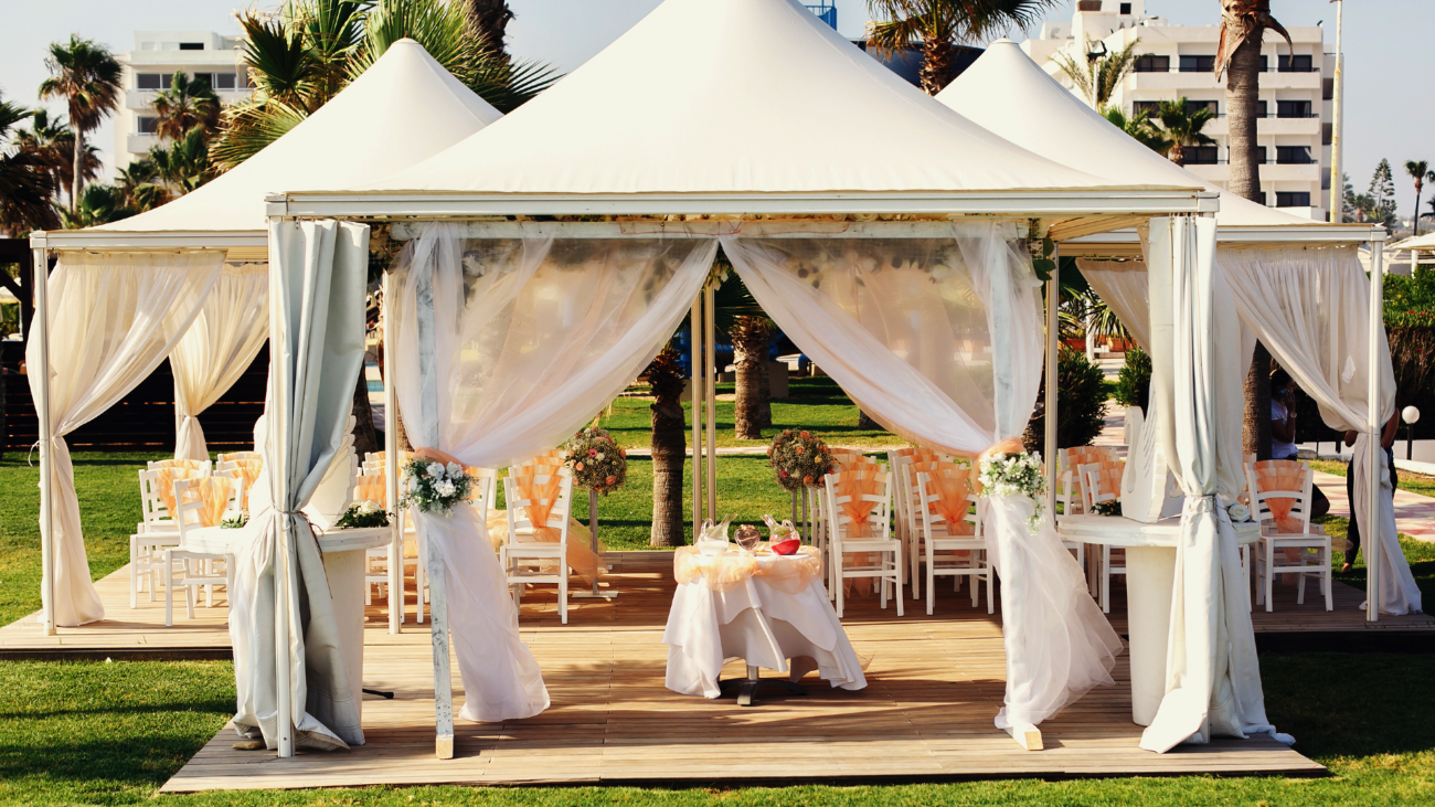 a luxurious wedding tent with haze peachy fabric and floral decorations near palm trees