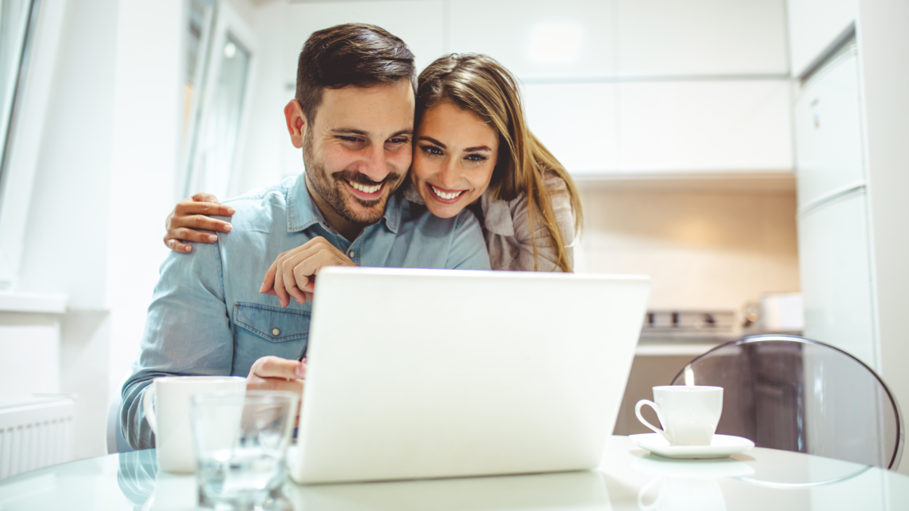 a man and woman look at a laptop computer screen and smile