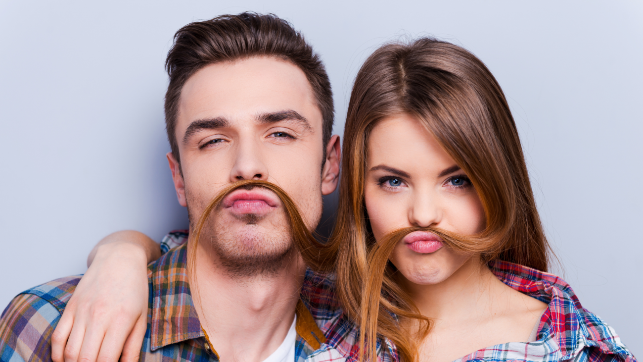 a man and woman wrap their arms around each other while the woman’s hair is covering her lip and the man’s lip to look like mustaches