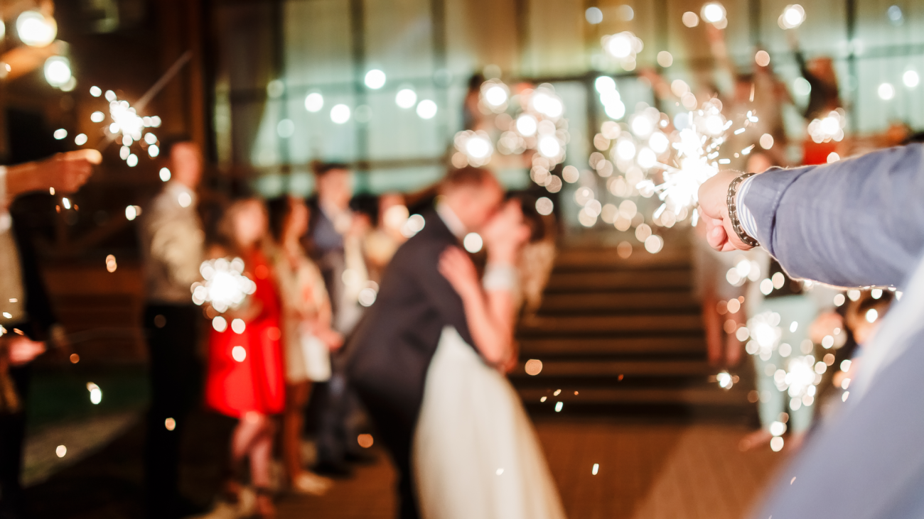 a newly married couple kiss on their wedding day as guests hold sparklers in celebration