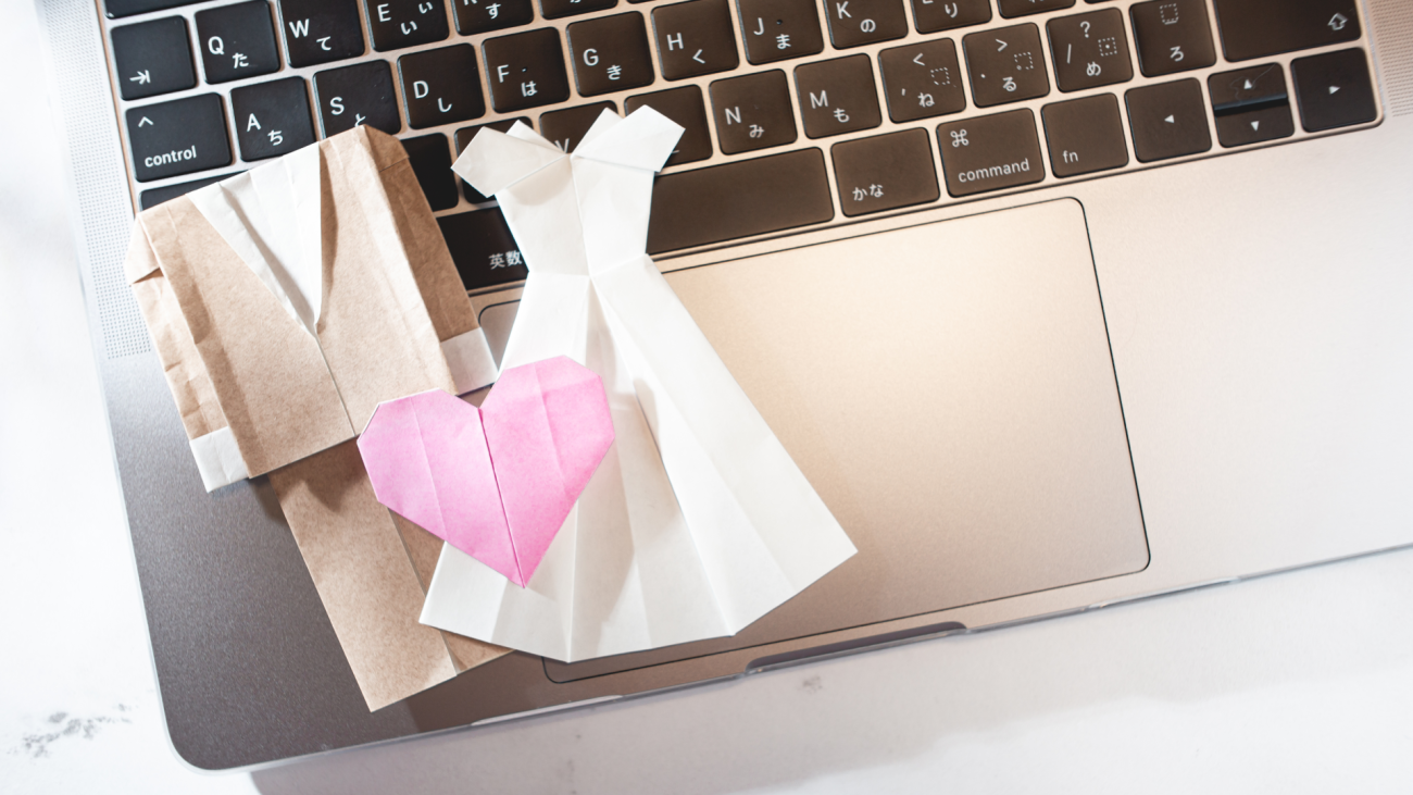 a paper bride and groom sit on top of a laptop computer keyboard