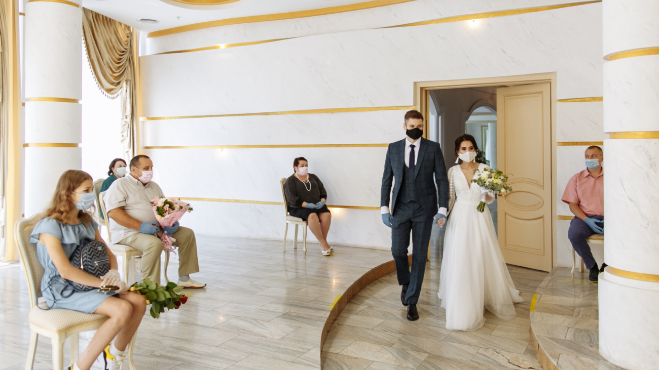 a social distanced wedding where a masked bride, groom, and guests are in attendance