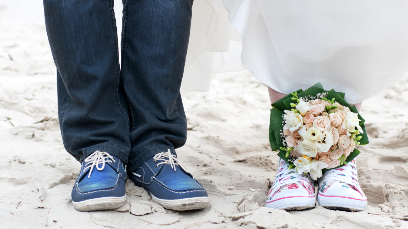 a wedding couple on a beach wearing sneakers with a bouquet on the bride’s sneakers