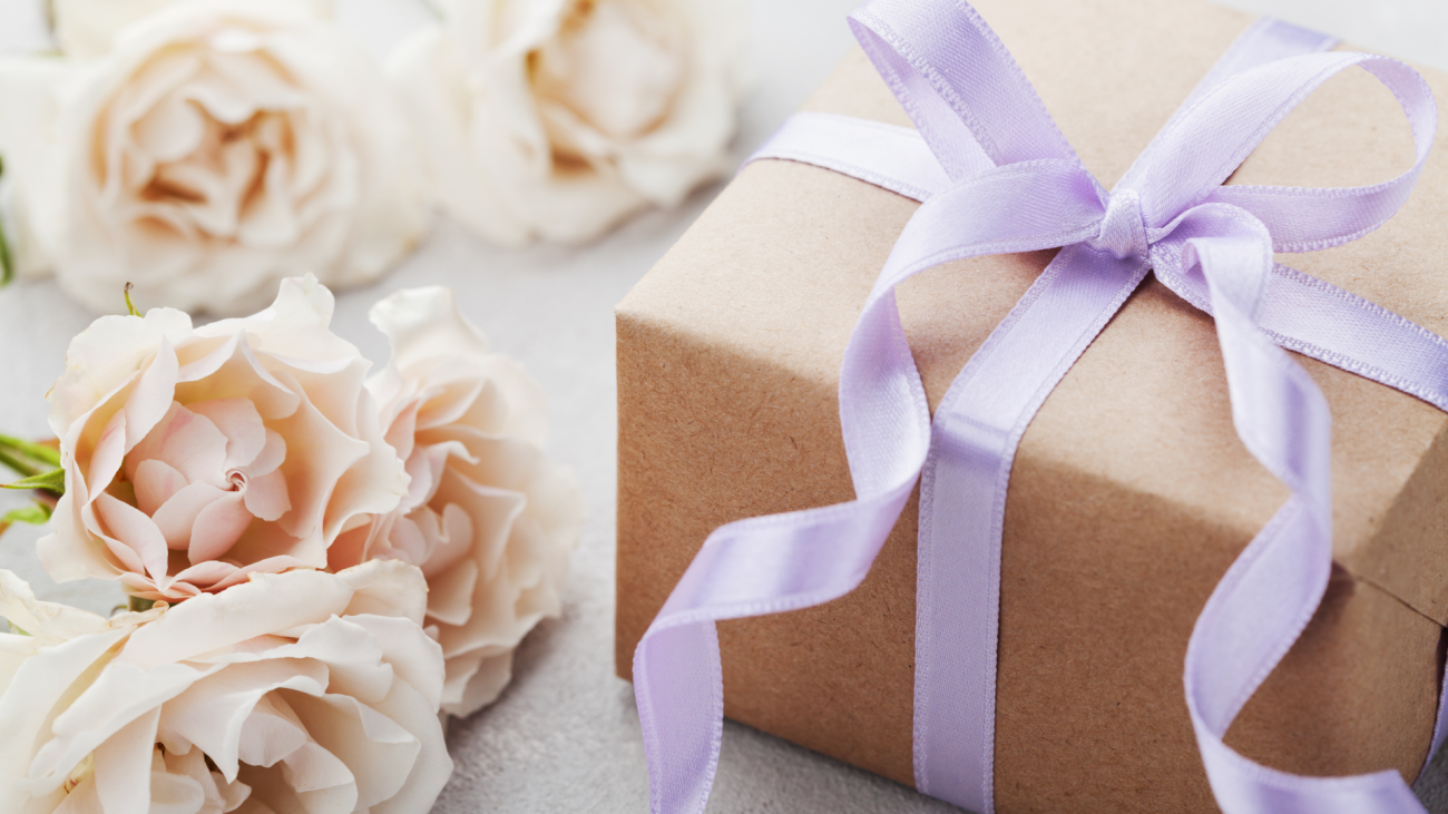 a wedding gift wrapped in brown paper and a purple ribbon sitting next to flowers