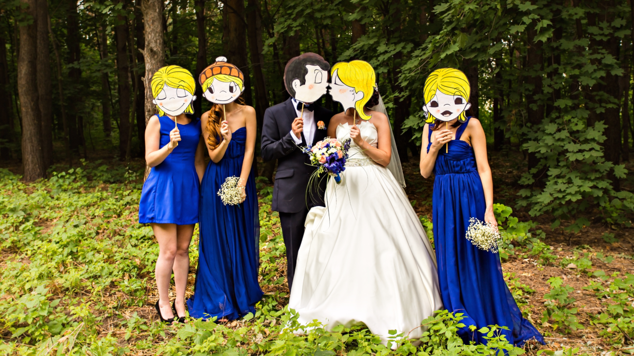 a wedding party holding up cartoon mask in front of their faces outdoors
