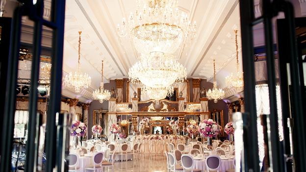 an empty wedding reception hall with a chandelier hanging from a ceiling, chairs, and tables with bouquets of flowers on top