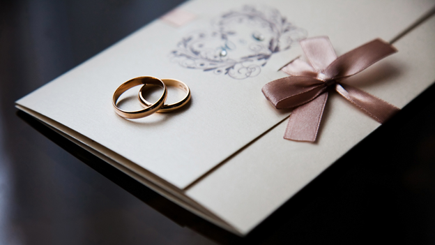 wedding rings sit on top of a traditional wedding invitation card