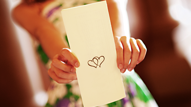 a woman holding a wedding program with two hearts on display