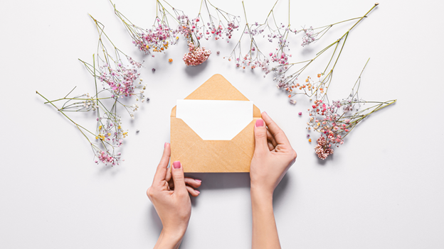 a woman opens a wedding invitation or save the date from an envelope, which is surrounded by flowers on a white background