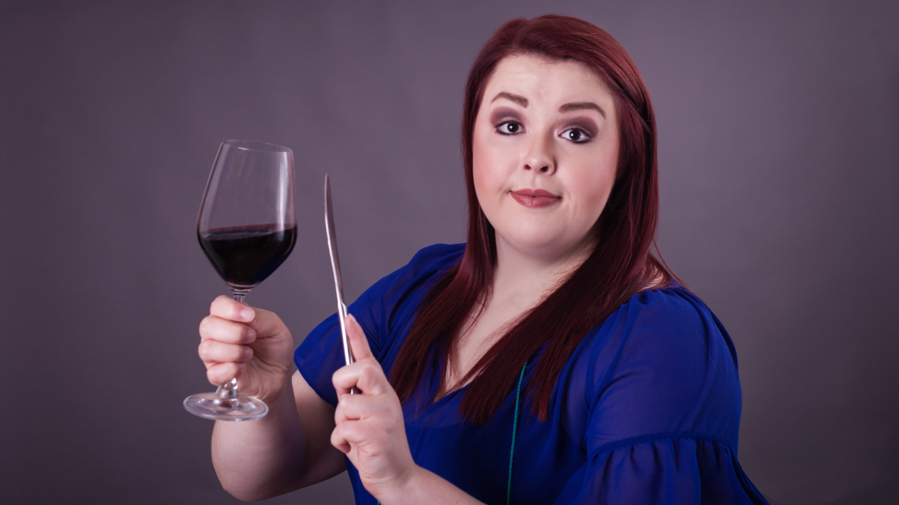 a woman trying to get attention by clinking butter knife against glass of red wine