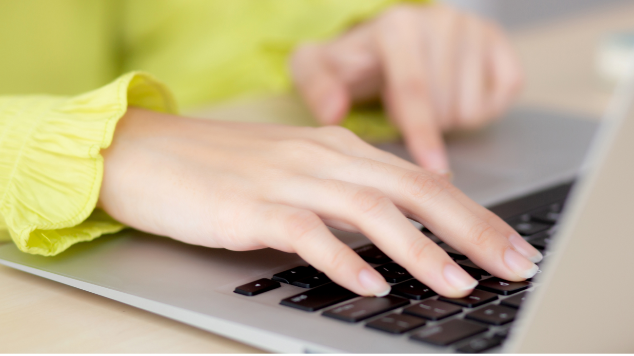 a woman’s hands type on a laptop keyboard