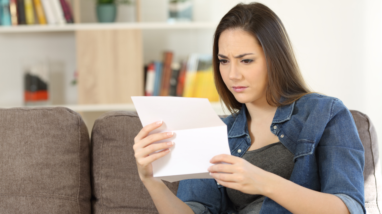 a worried woman reads a letter while sitting on a couch in her living room at home