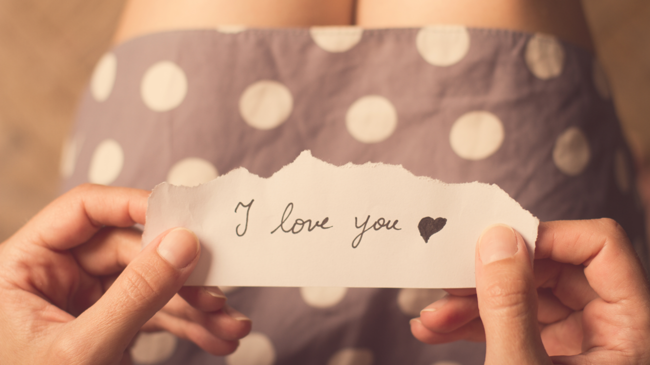 top view of woman in a dotted dress holding a paper message with the text ‘I love you’