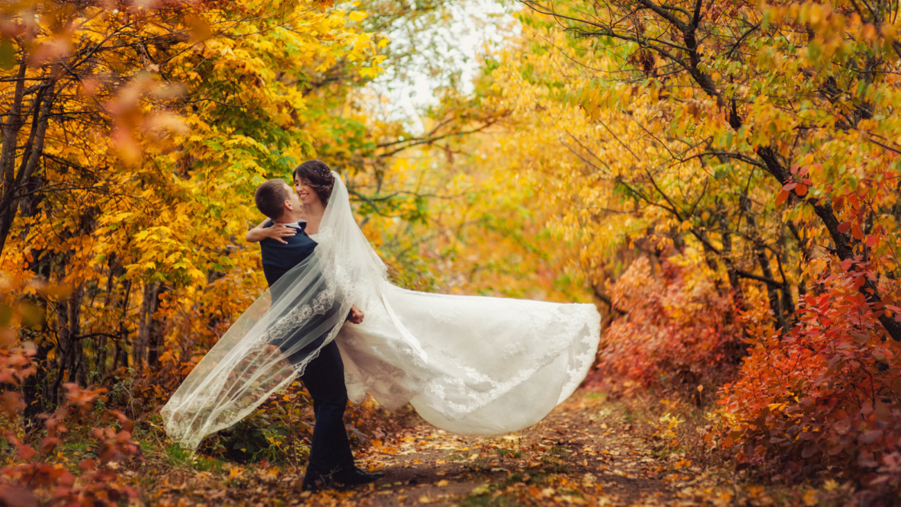 a bride and groom are twirling in a fall setting surrounded by trees