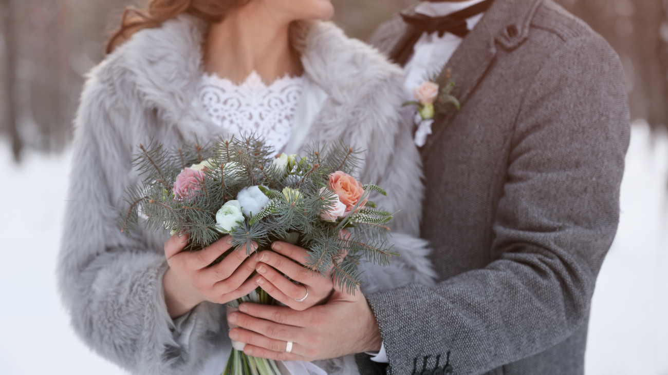 Newlywed couple holds bouquet of flowers in the snow