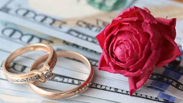 two wedding rings and a rose sit on top of 100-dollar bills