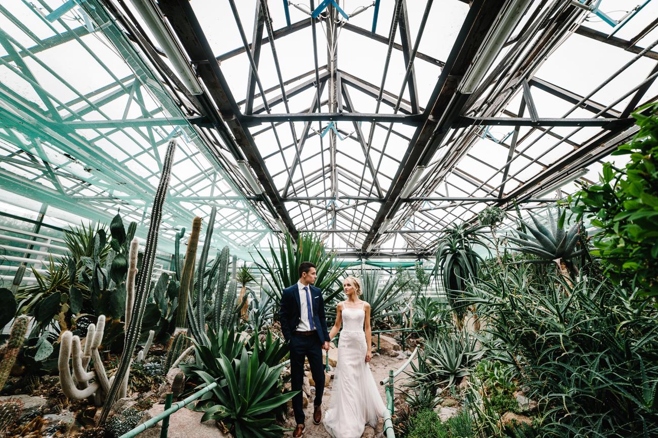 Bride and groom surrounded by plants in a botanical garden.
