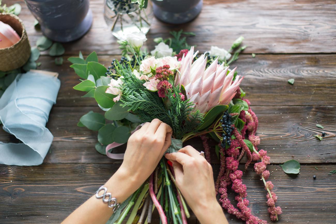 Woman tying together wedding bouquet of different flowers.