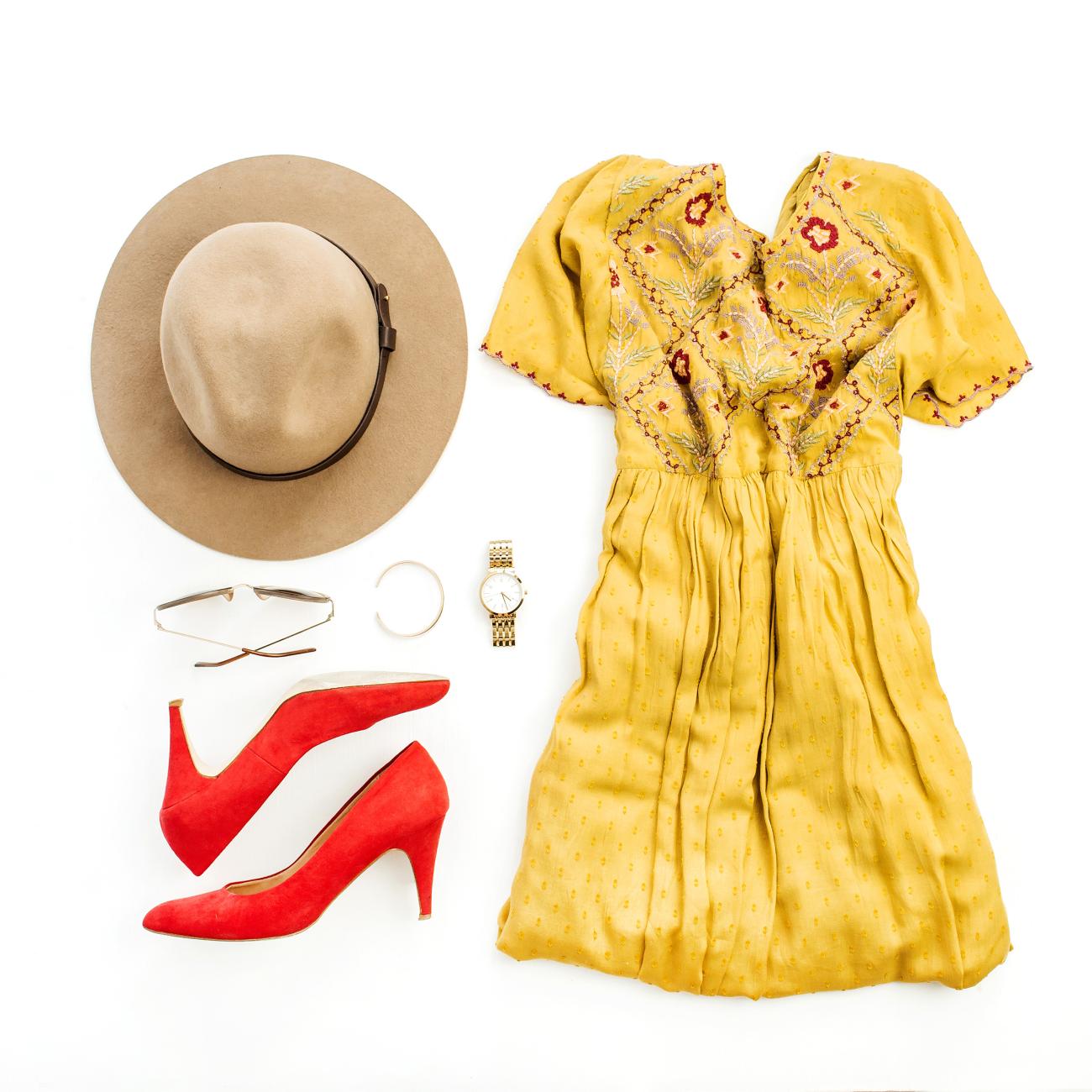 Flatlay with yellow dress, red shoes, brown hat, sunglasses, and a gold watch