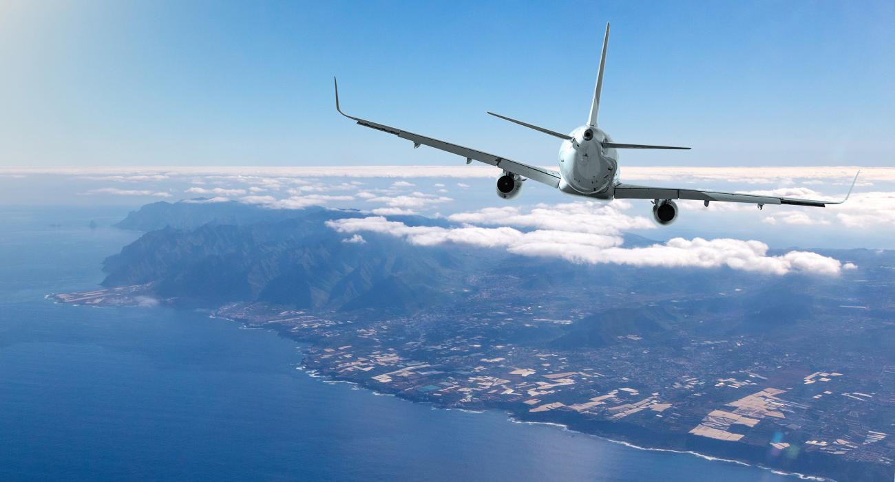 Airplane flying over ocean headed to a tropical island