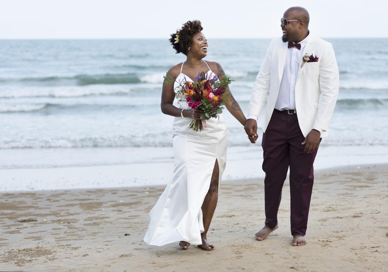 Barefoot bride and groom holding hands on the beach