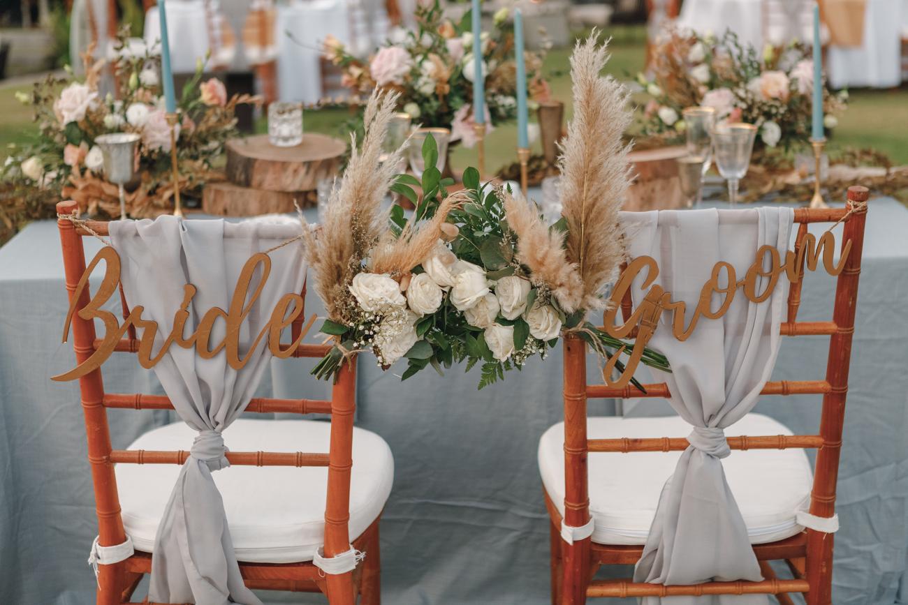 Wooden bride and groom chairs decorated with signs and flowers