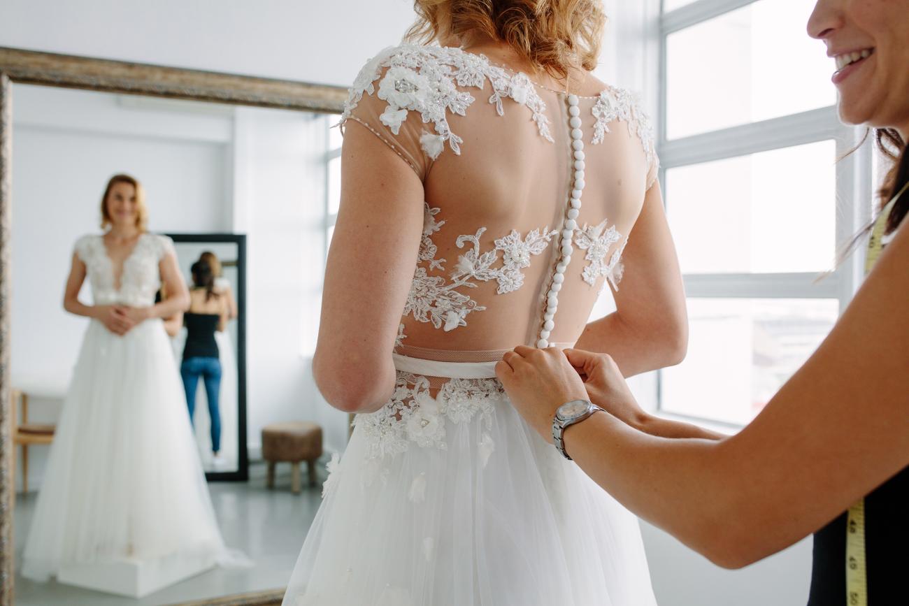 Bride getting the back of her wedding dress buttoned up by a tailor
