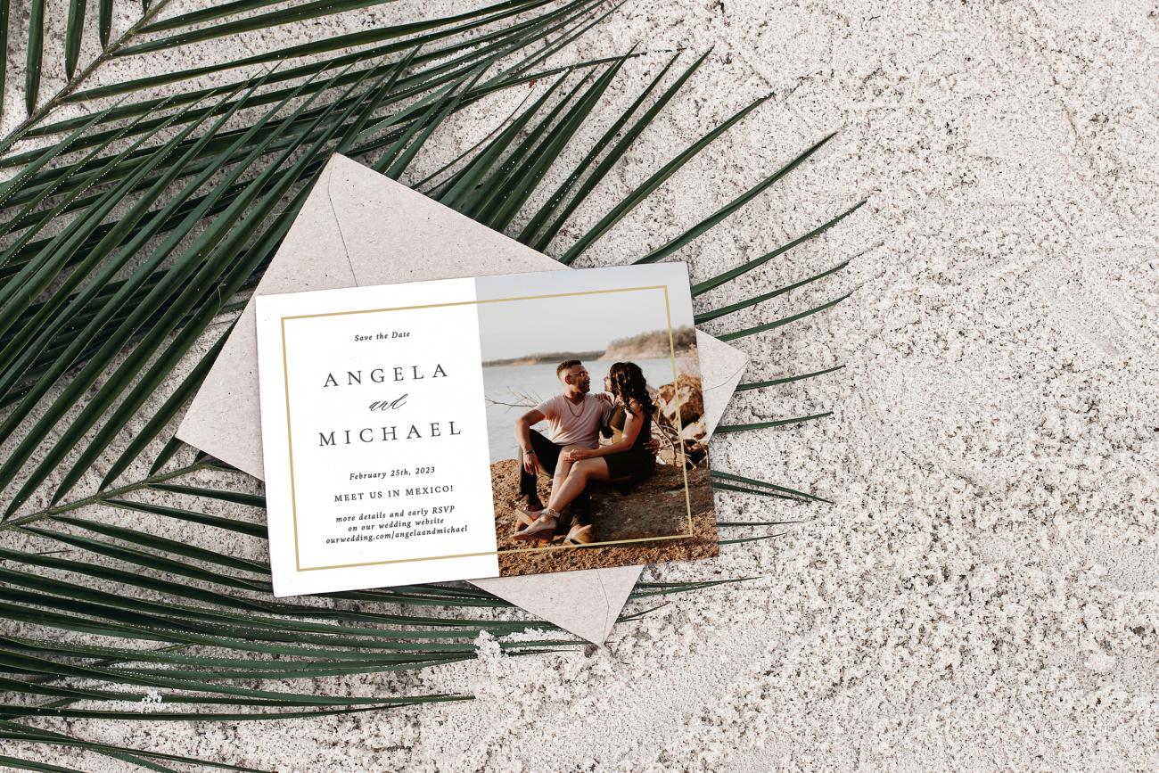 Save the date card and envelope laying on top of a palm leaf in the sand