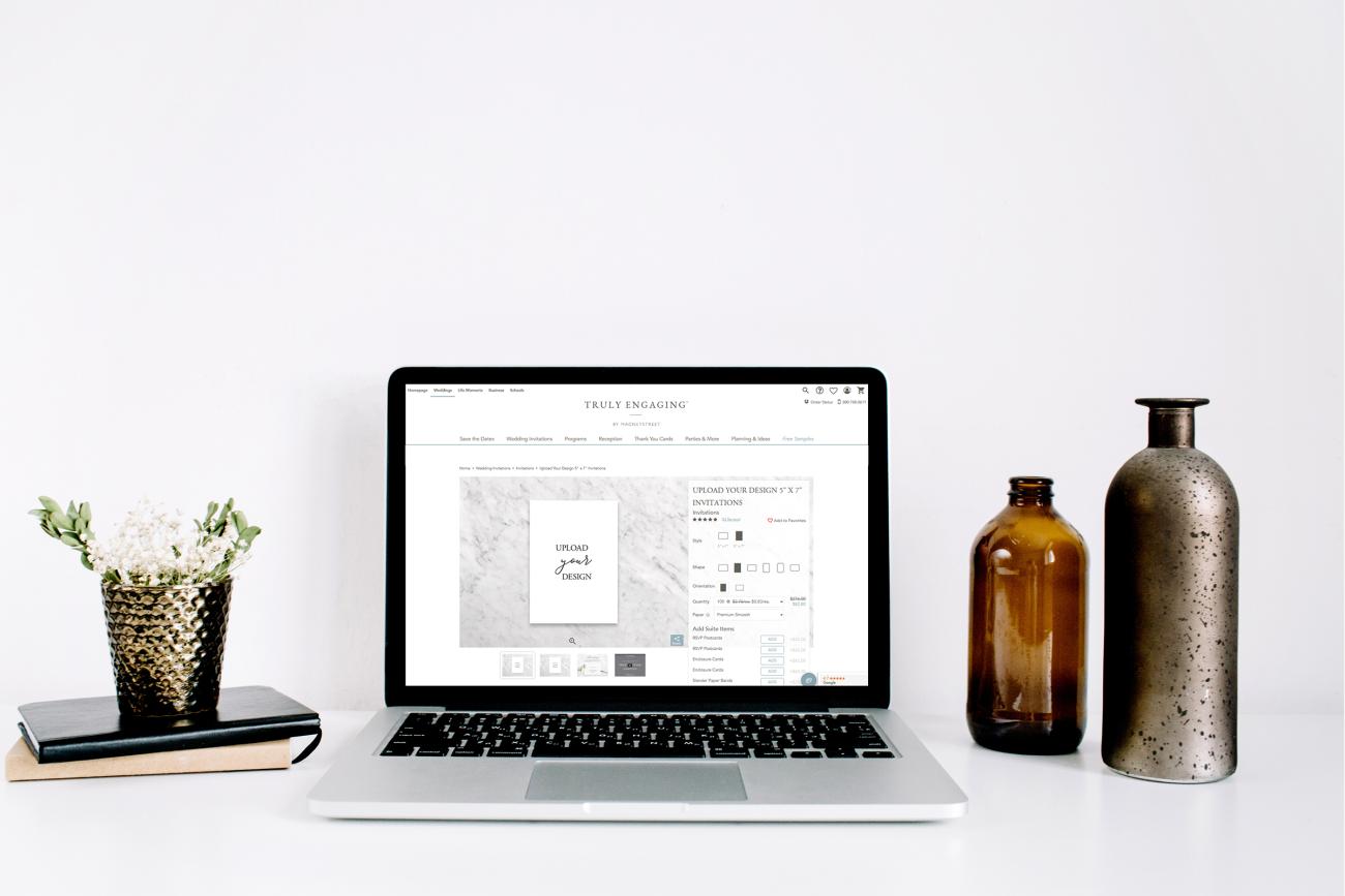 Laptop computer sitting on desk next to vases with upload your own design on the screen.