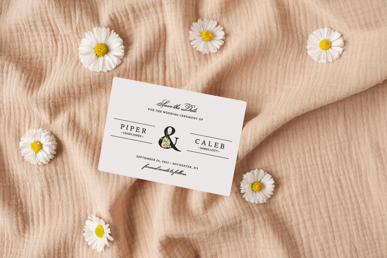 Save the date magnet laying on pink cloth surrounded by daisies