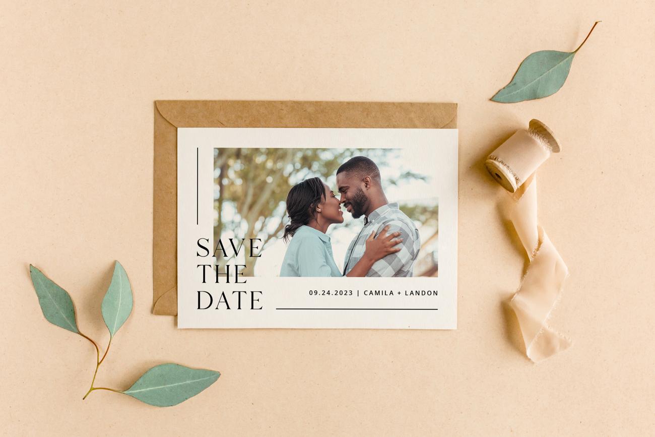 Flatlay of a save the date, green eucalyptus, and tan ribbon.