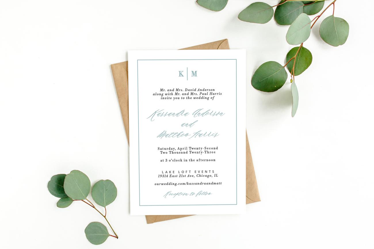 Wedding invitation on top of envelope next to green eucalyptus.